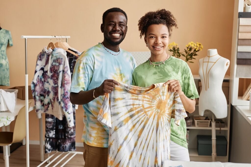 Two young successful designers holding tie dye t-shirt and looking at camera