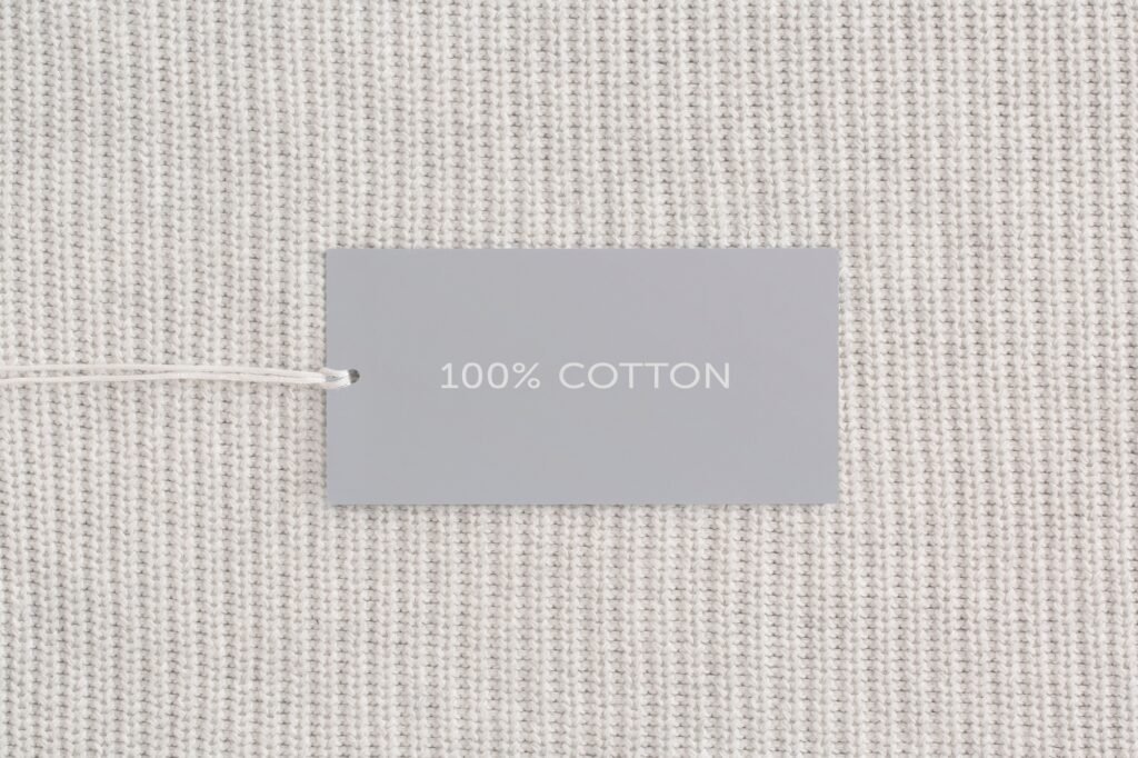 Clothes label with text 100% cotton on white textile closeup
