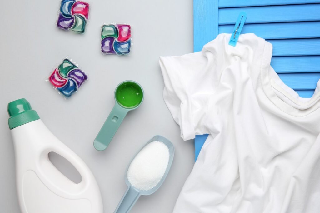 Different laundry detergents and t-shirt on grey background, flat lay